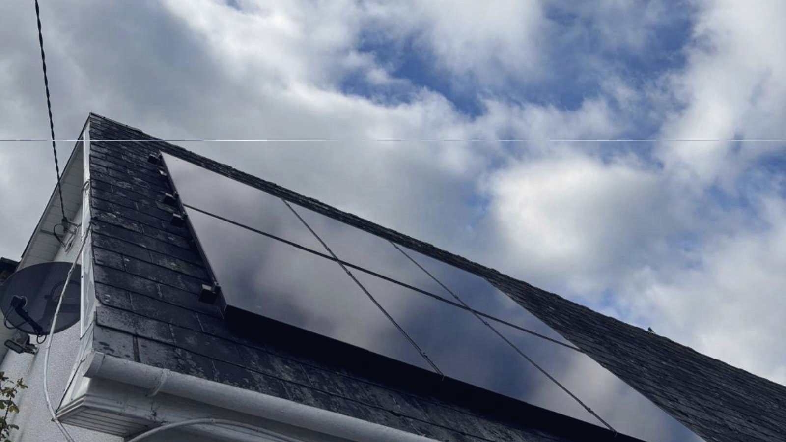 All-black solar panels on a slate roof under a bright, cloudy Irish sky
