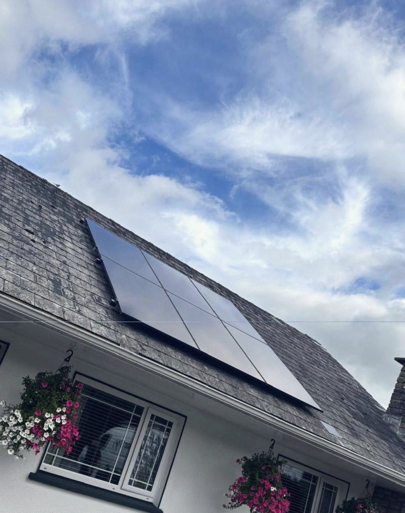 The front of a Midlands home with hanging baskets, and all-black panels on the slate roof above