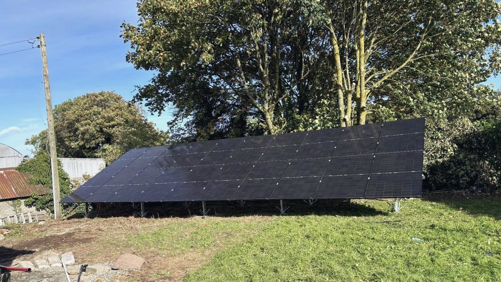 Twenty black solar panels on a galvanised ground-mount frame on a lawn, with trees behind