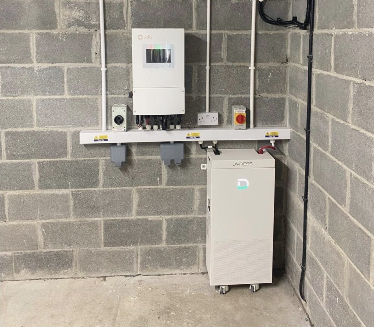 The whole plant wall: Solis inverter, AC and DC isolators, labelled trunking, the Dyness battery and the cable run to the board