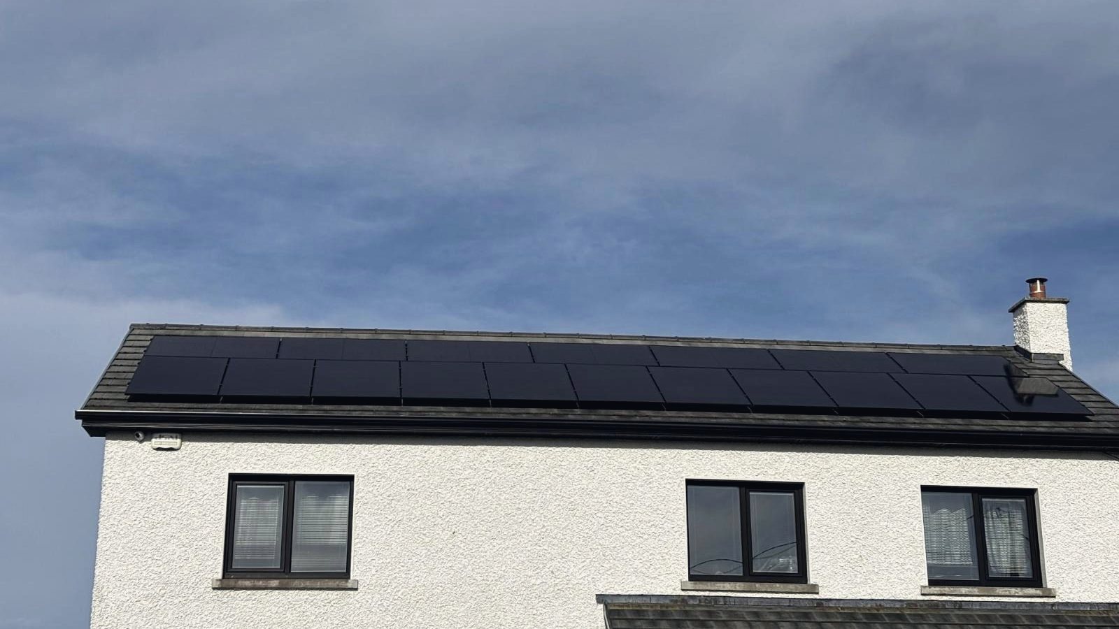 A white two-storey house with a row of all-black solar panels along its tiled roof