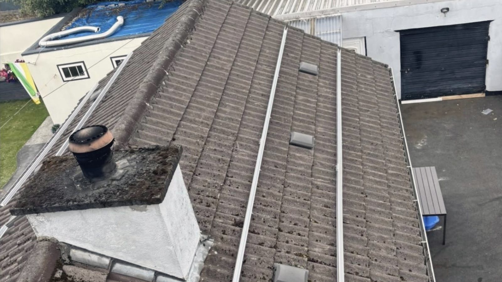 Aluminium mounting rails fixed in straight runs down a tiled roof beside the chimney, before the panels go on